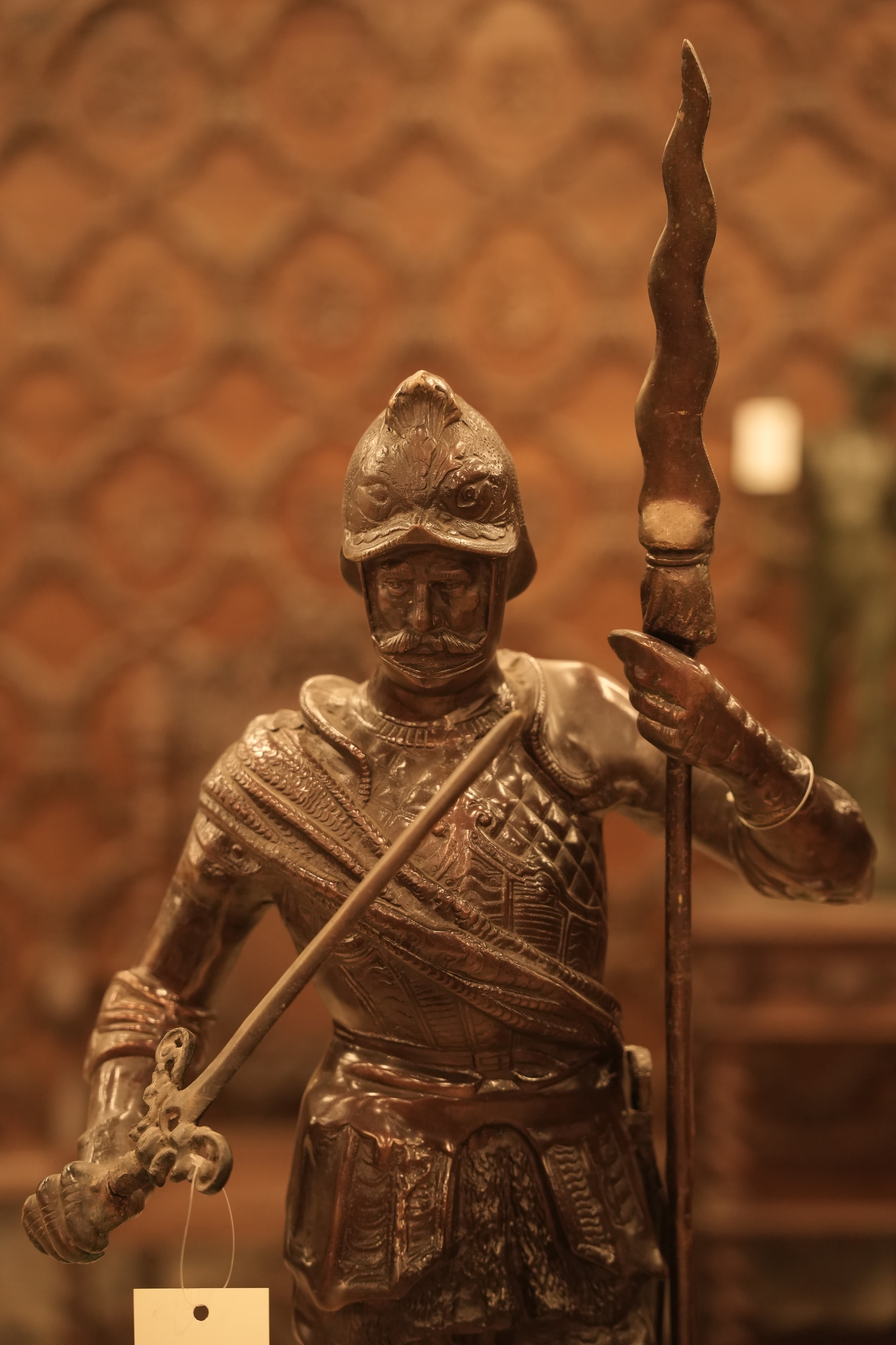 This is a large, bronze-finish brass statue depicting a 16th-17th century style soldier or Roman warrior holding a spear and sword.